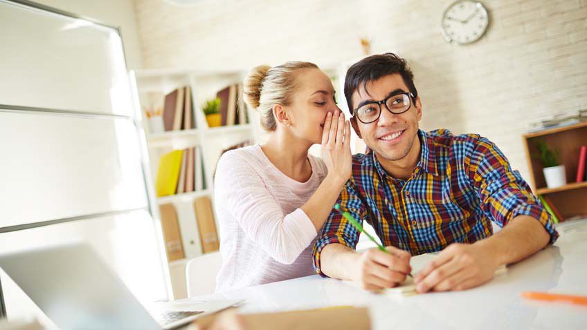 Teenage girl whispering fun to attractive groupmate